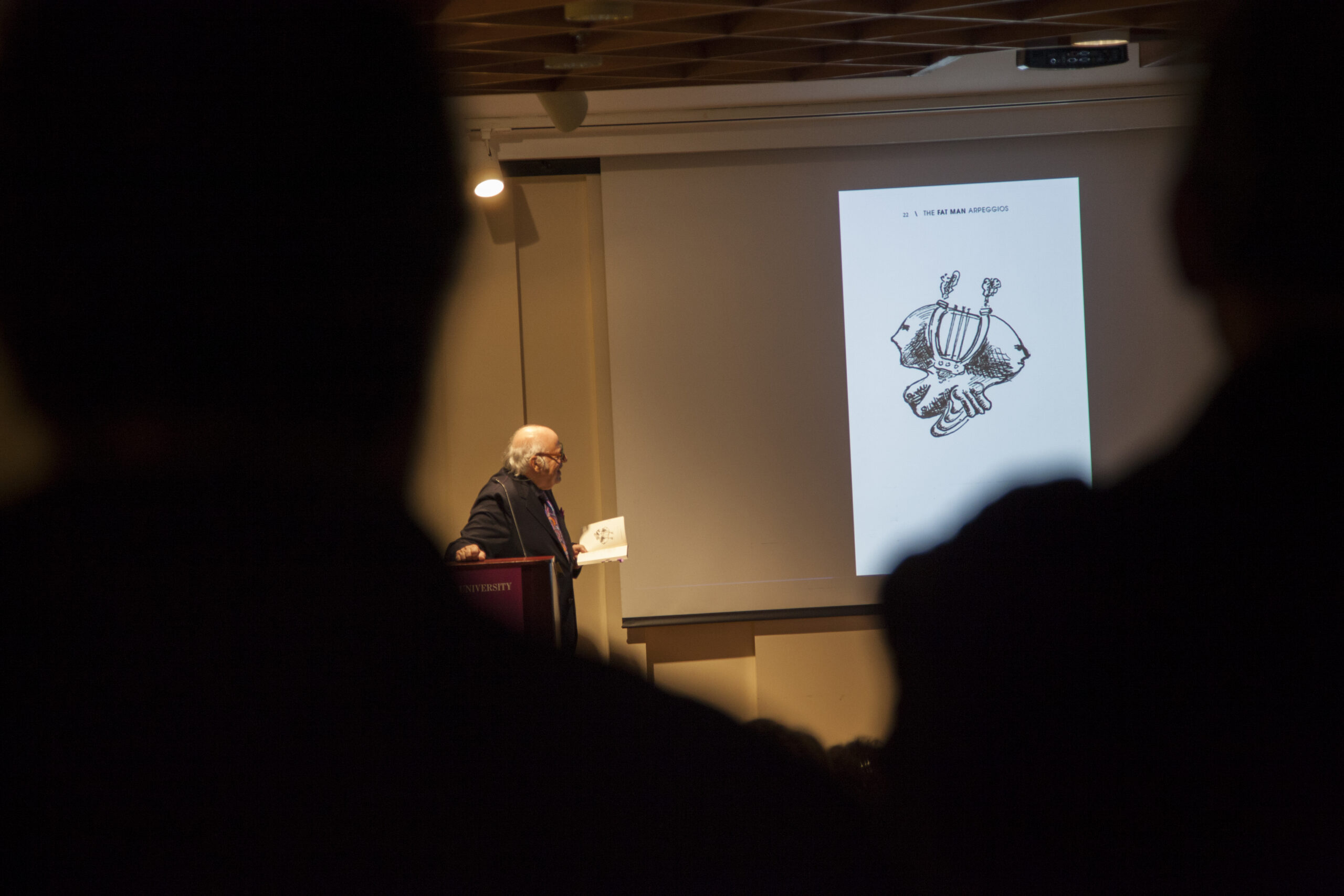 author-showing-image-on-projector-screen-from-diffraction-exhibition-opening-and-the-fat-man-arpeggios-book-pres-at-casa-italiana