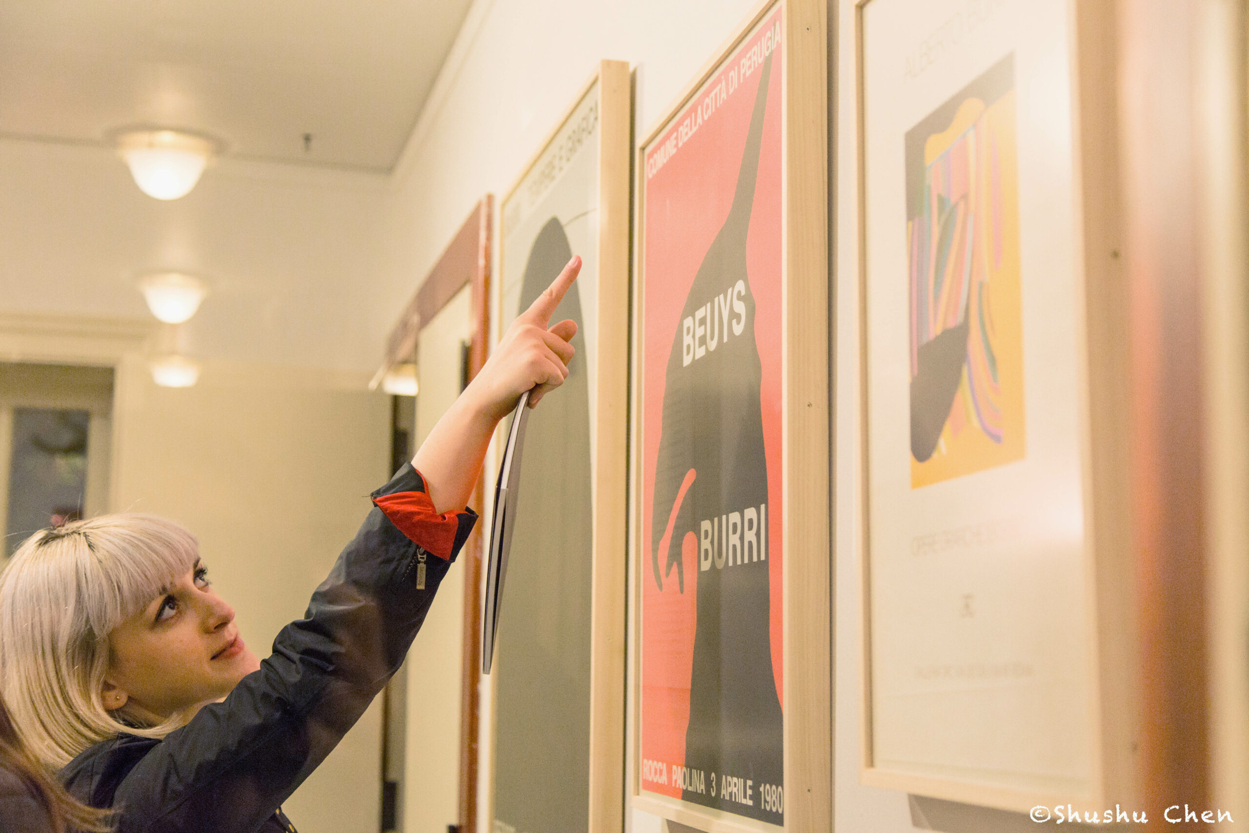 woman-pointing-at-artworks-on-wall-from-exhibition-opening-burri-posters-at-casa-italiana