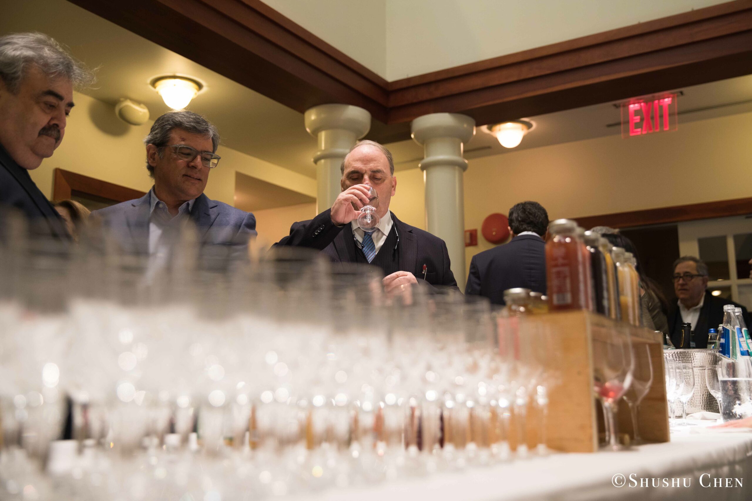 a-man-in-a-suit-tasting-whiskey-at-a-bar-surrounded-by-other-men-observing-from-Italian-table-talks-at-casa-italiana