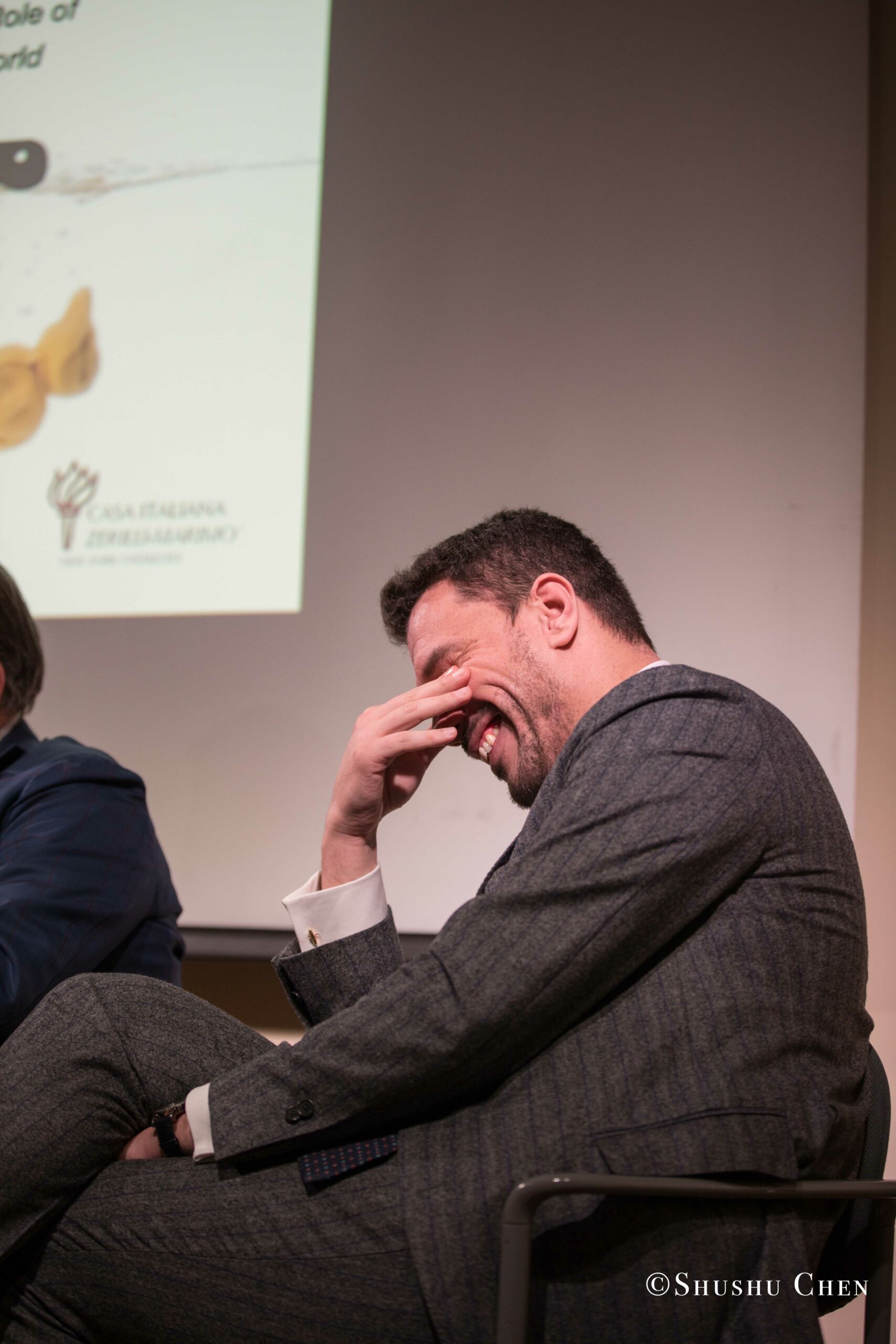 a-man-in-a-grey-suit-sits-laughing-with-his-hand-covering-his-face-from-Italian-table-talks-at-casa-italiana