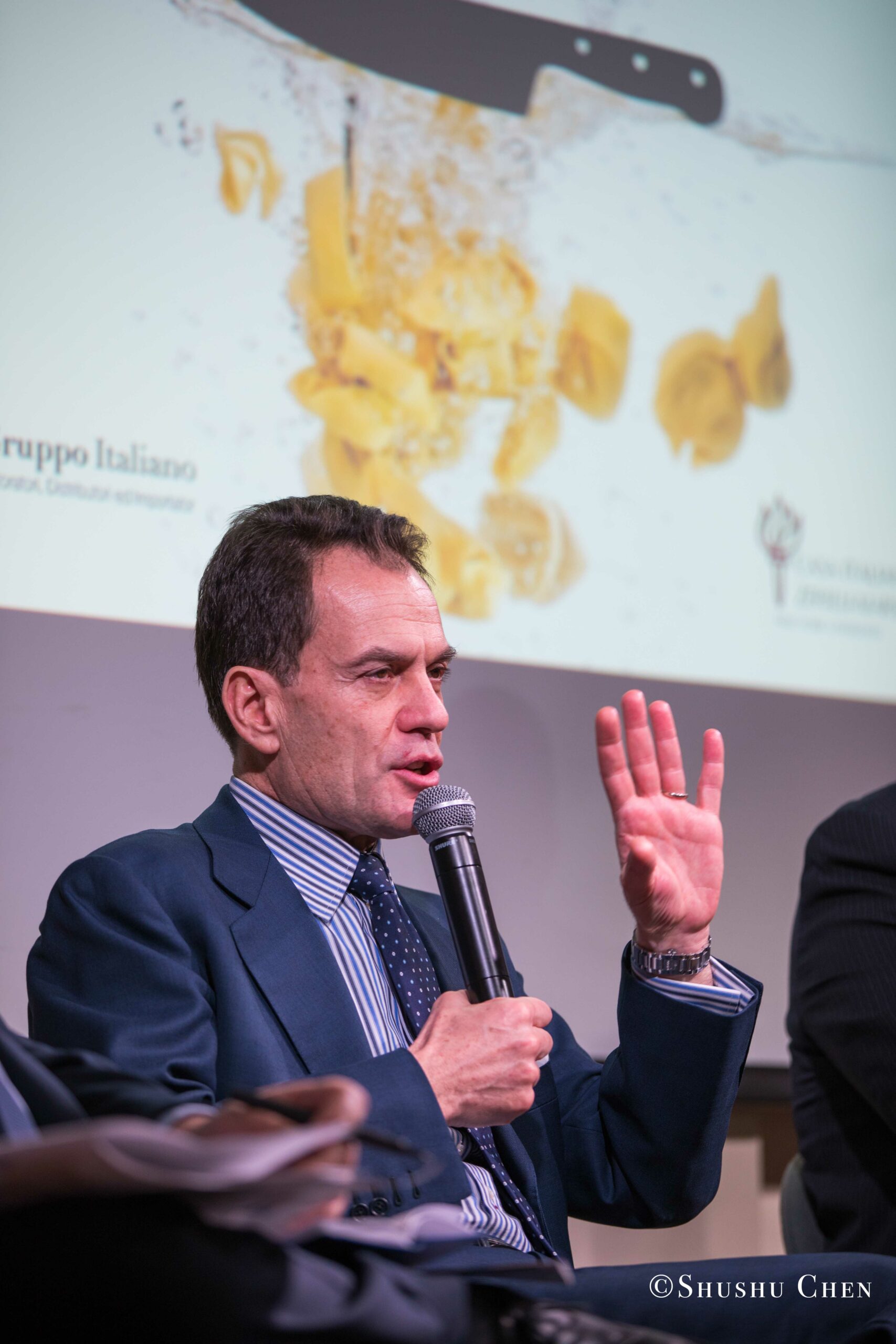a-man-in-a-dark-suit-and-tie-speaking-from-Italian-table-talks-at-casa-italiana