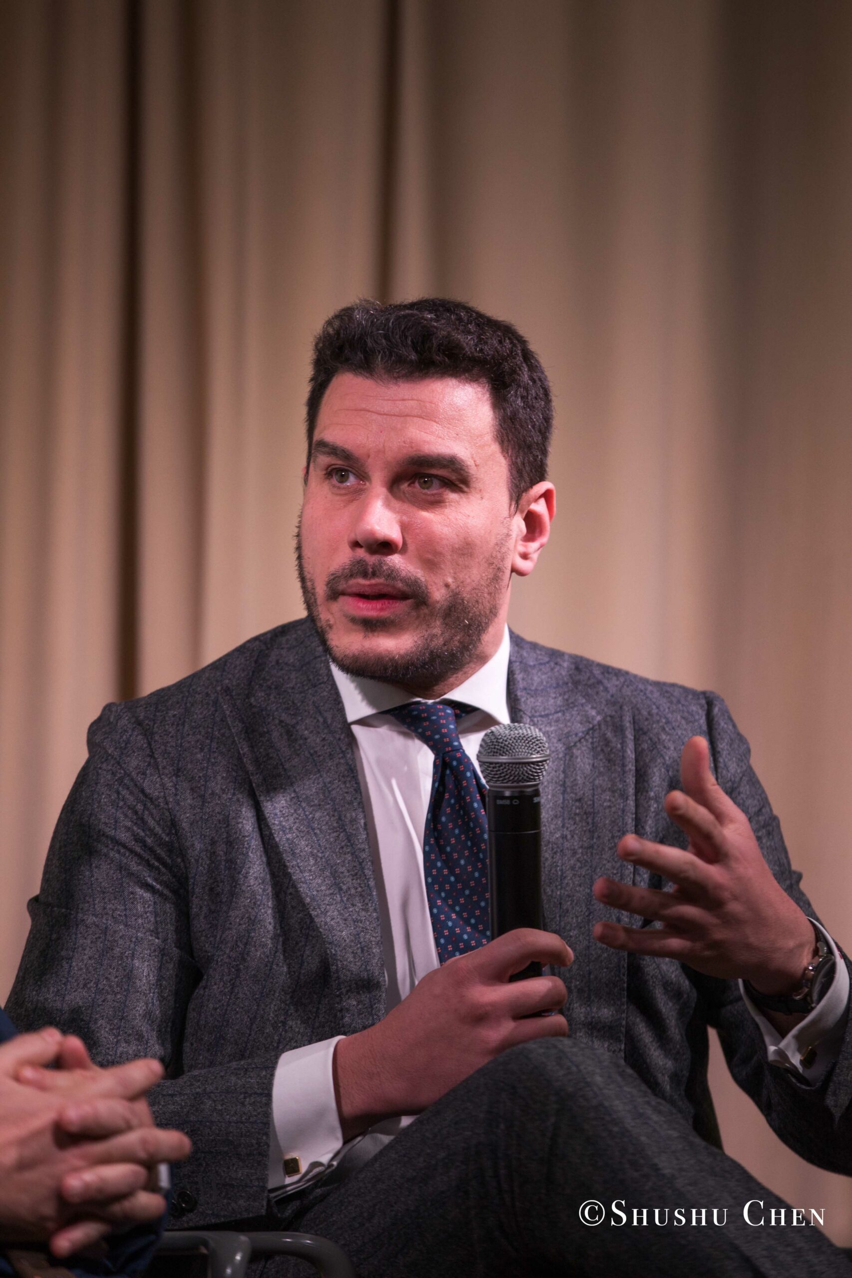 a-man-in-a-gray-suit-and-blue-tie-speaking-from-Italian-table-talks-at-casa-italiana