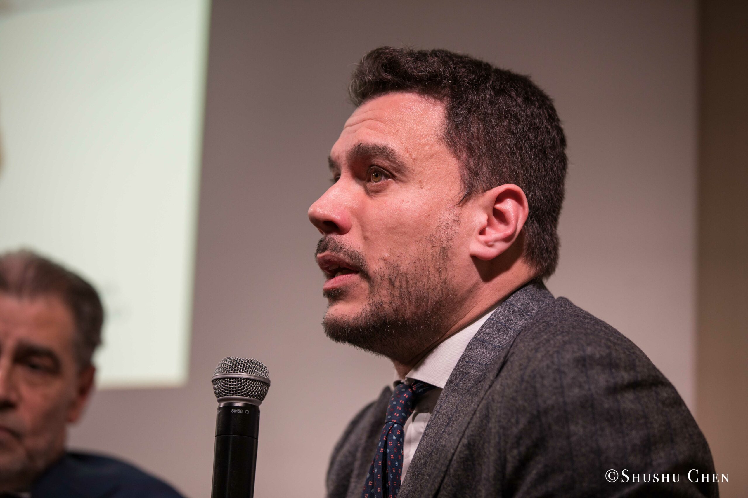 a-man-in-a-gray-suit-and-patterned-tie-speaking-from-Italian-table-talks-at-casa-italiana
