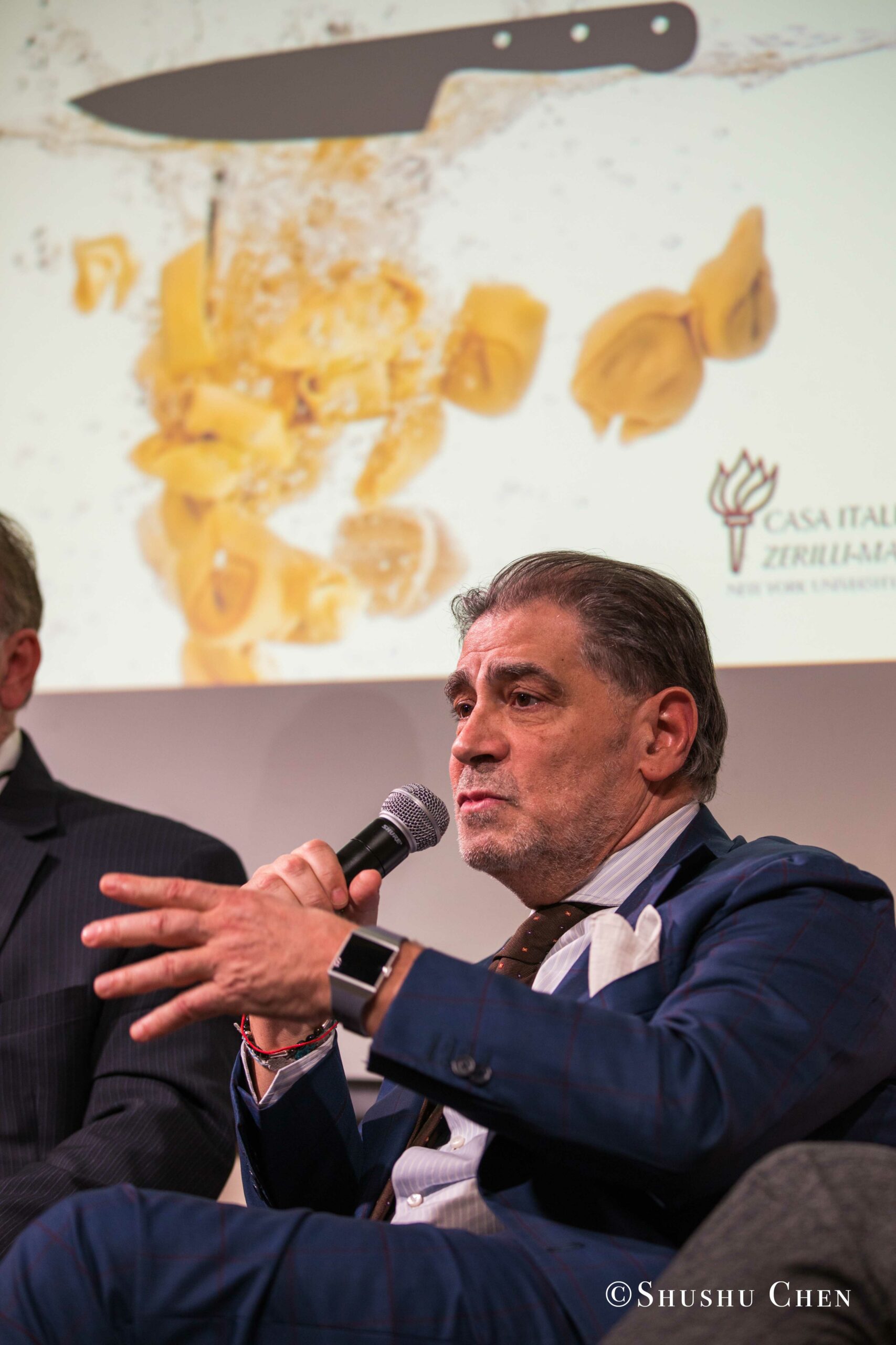 a-middle-aged-man-in-a-blue-suit-speaking-from-Italian-table-talks-at-casa-italiana