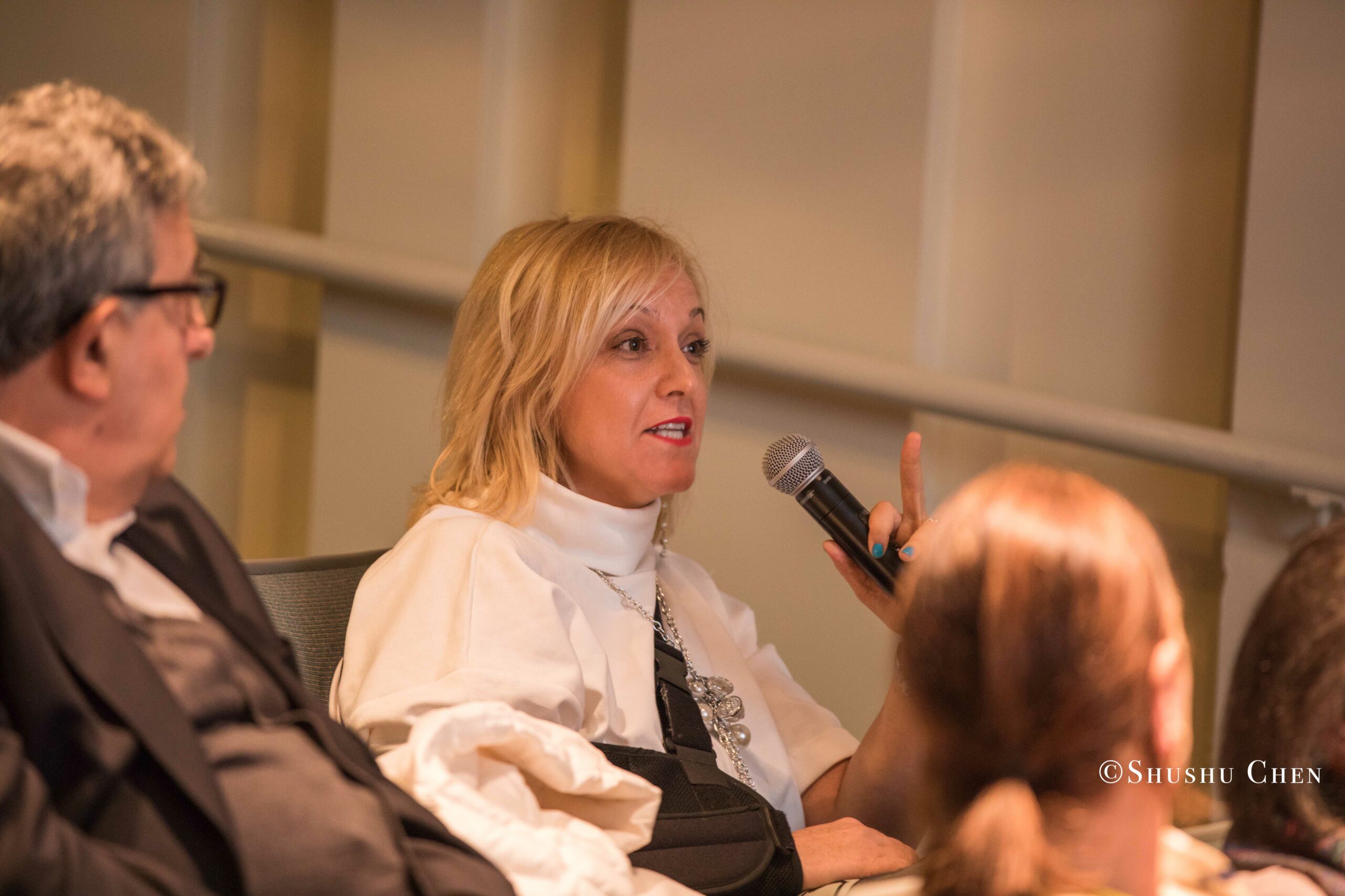 a-woman-speaks-into-a-microphone-at-an-event-from-Italian-table-talks-at-casa-italiana