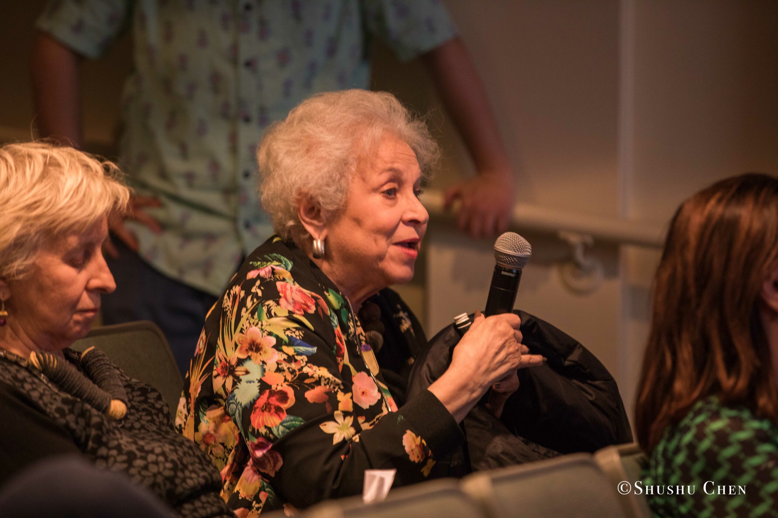 elderly-woman-with-white-hair-speaking-into-a-microphone-from-Italian-table-talks-at-casa-italiana
