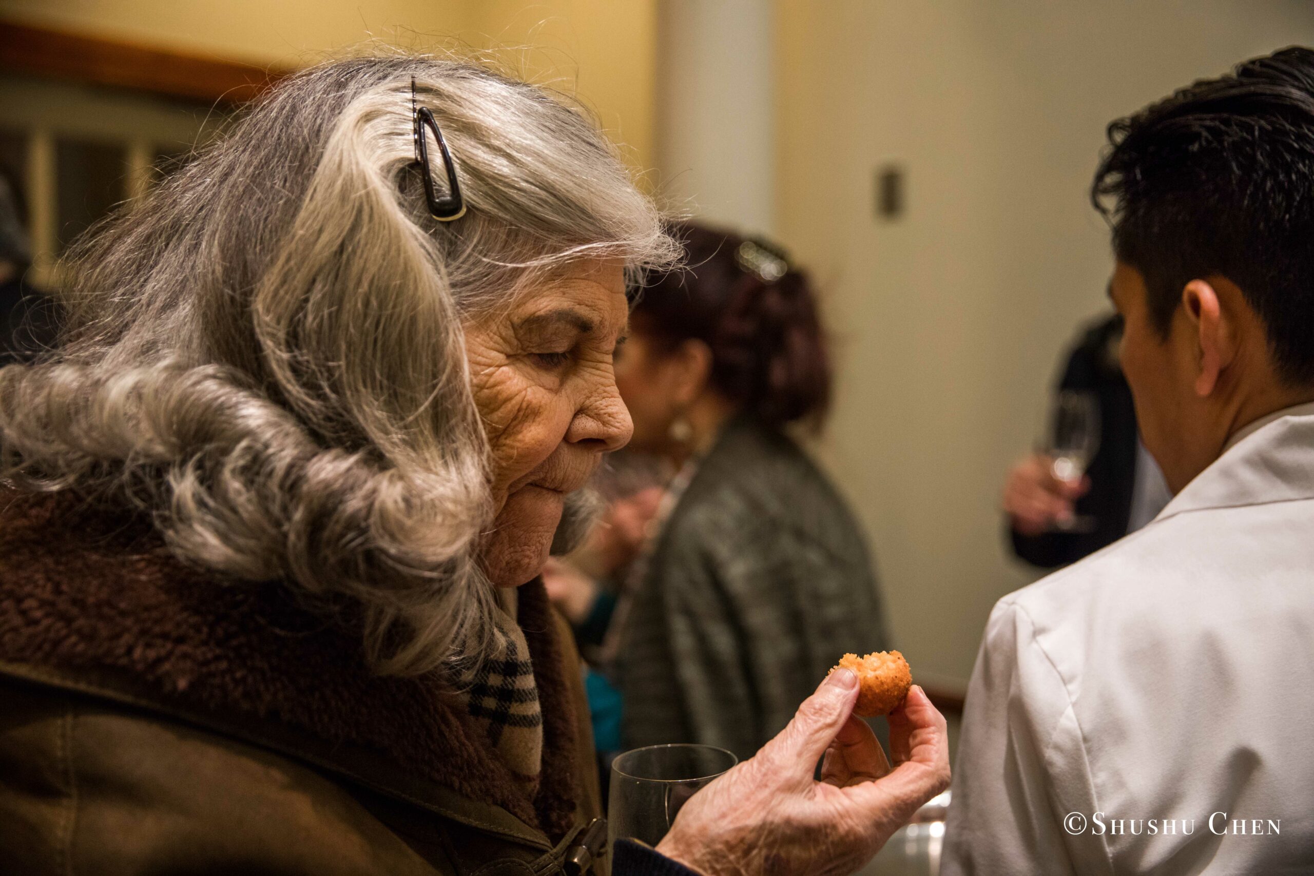 an-elderly-woman-with-gray-hair-and-glasses-observes-a-pastry-in-her-hand-from-Italian-table-talks-at-casa-italiana