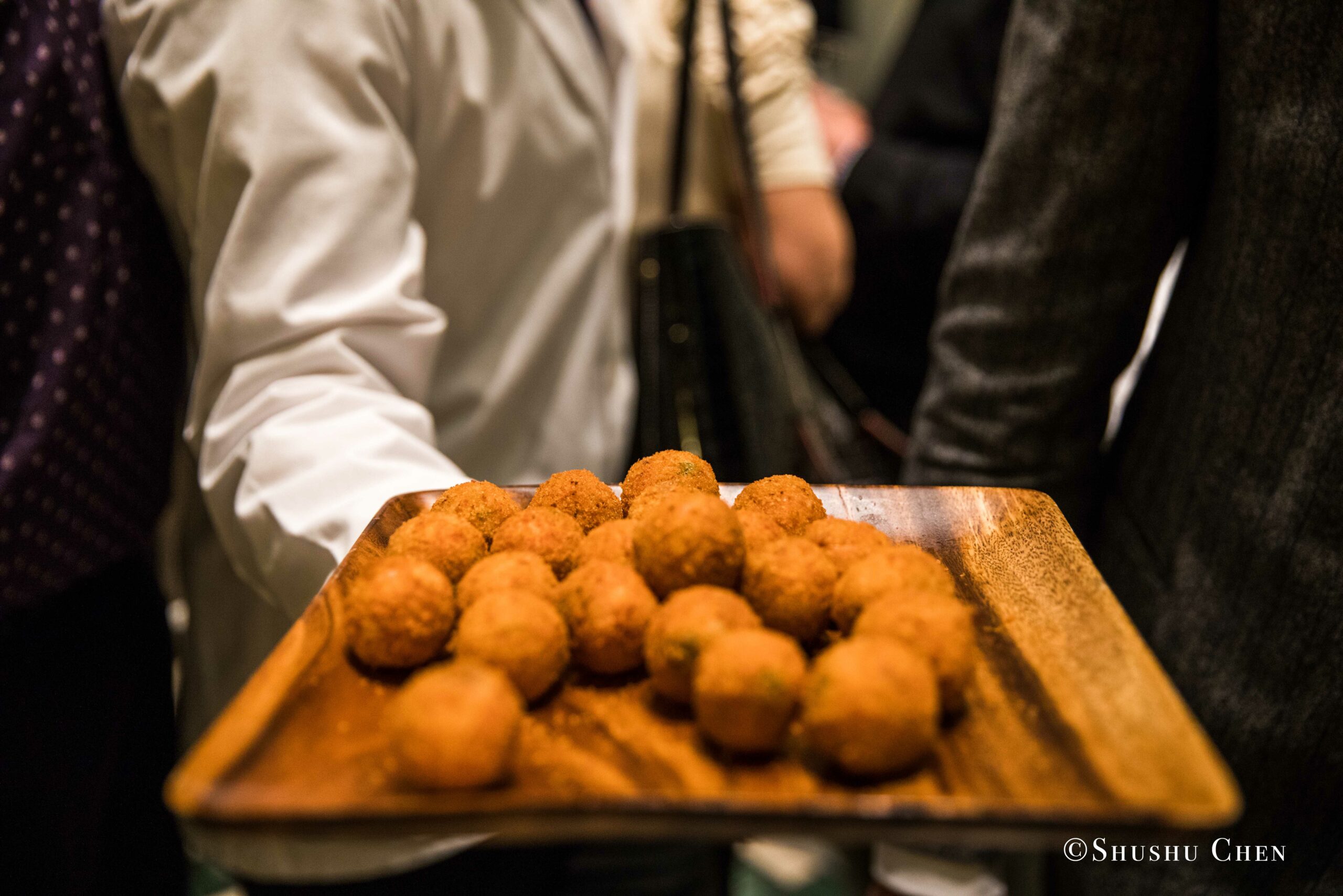 a-waiter-holding-a-wooden-tray-of-golden-brown-arancini-balls-from-Italian-table-talks-at-casa-italiana