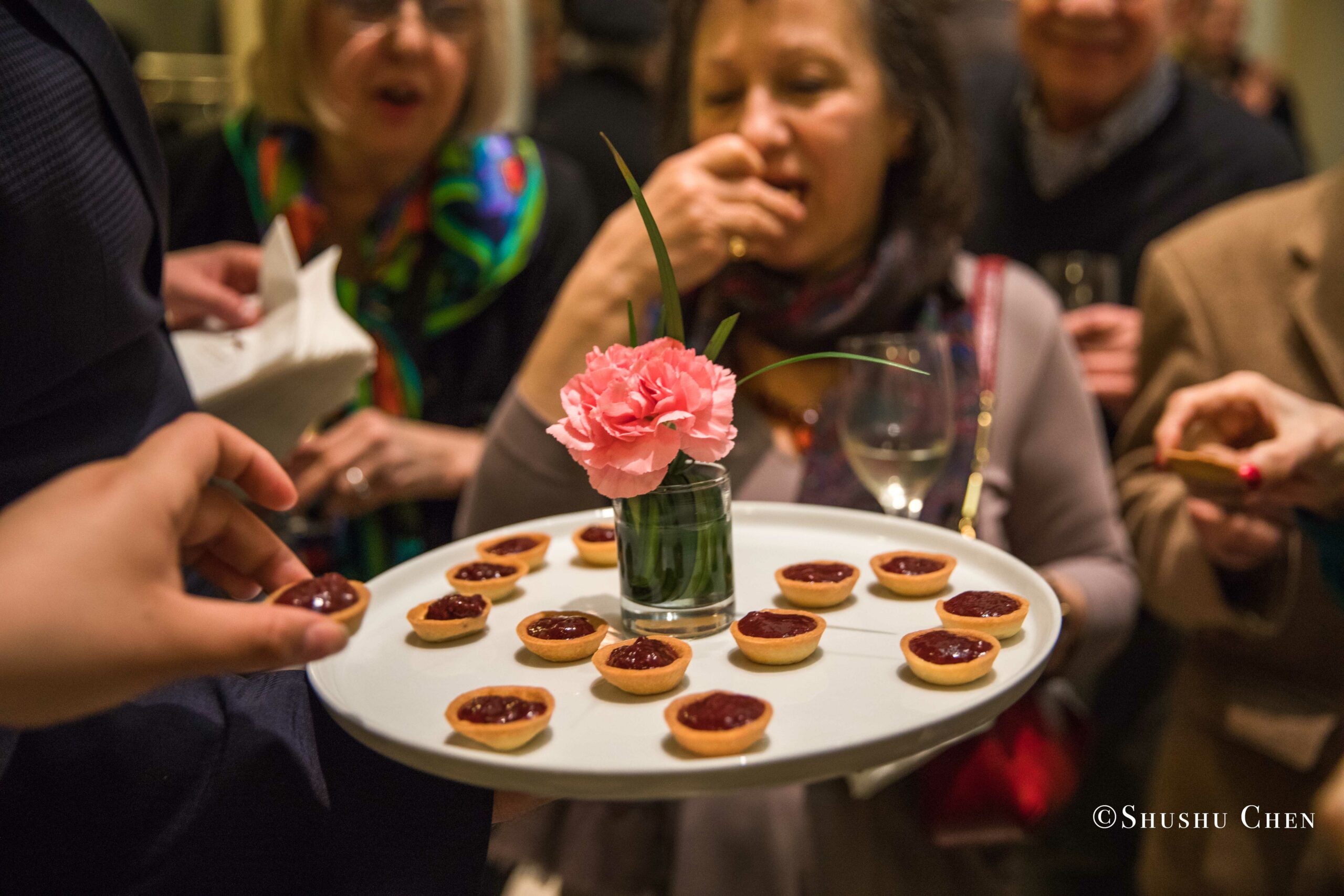 a-server-holding-a-tray-of-elegant-appetizers-with-a-pink-flower-in-a-small-vase-offering-them-to-a-group-of-guests-from-Italian-table-talks-at-casa-italiana